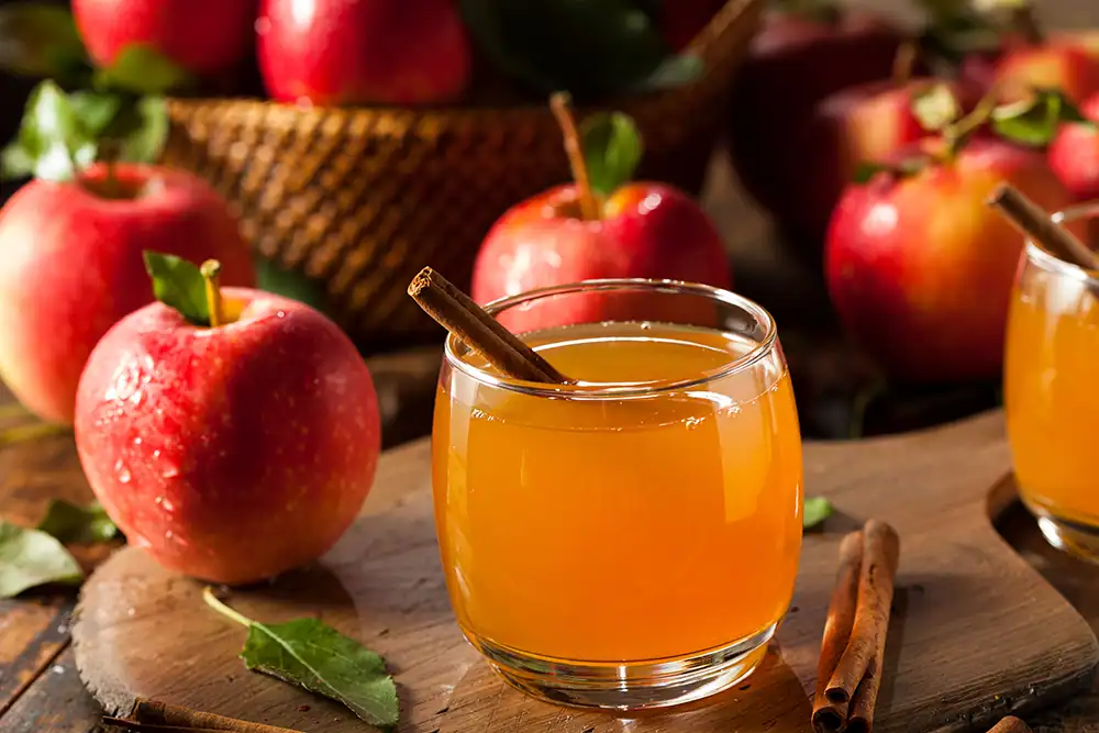 Glass of cider with cinnamon stick garnish with apples in background.