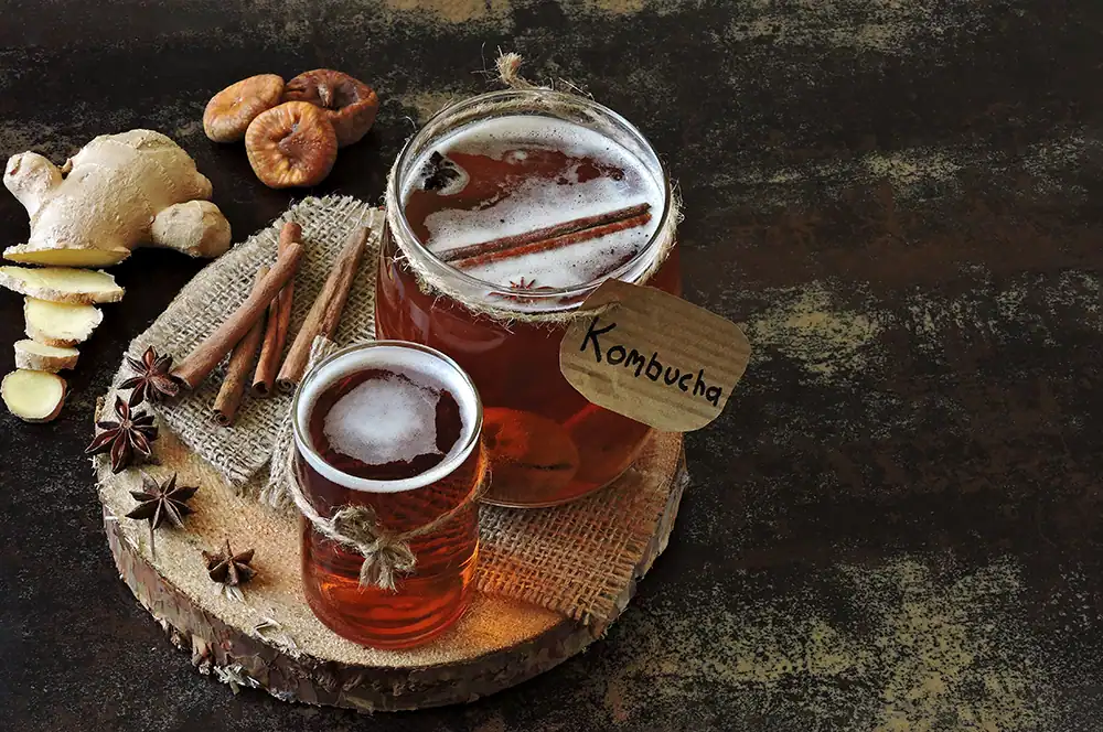 Jelly jars filled with Kombucha on a platter with cinnamon sticks.