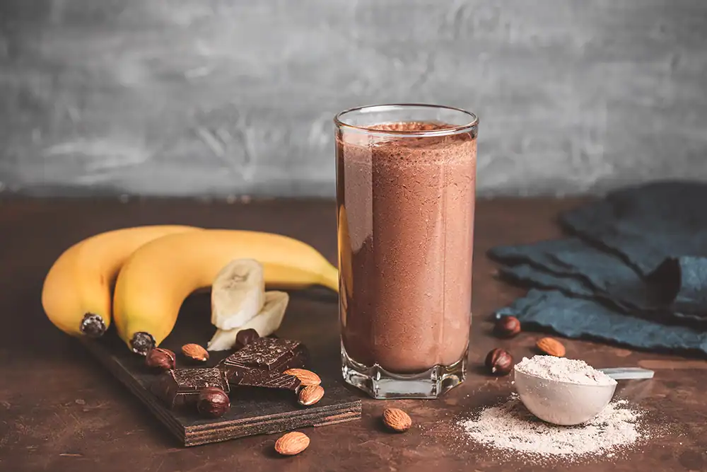 A glass of chocolate milk with bananas and a chocolate bar.