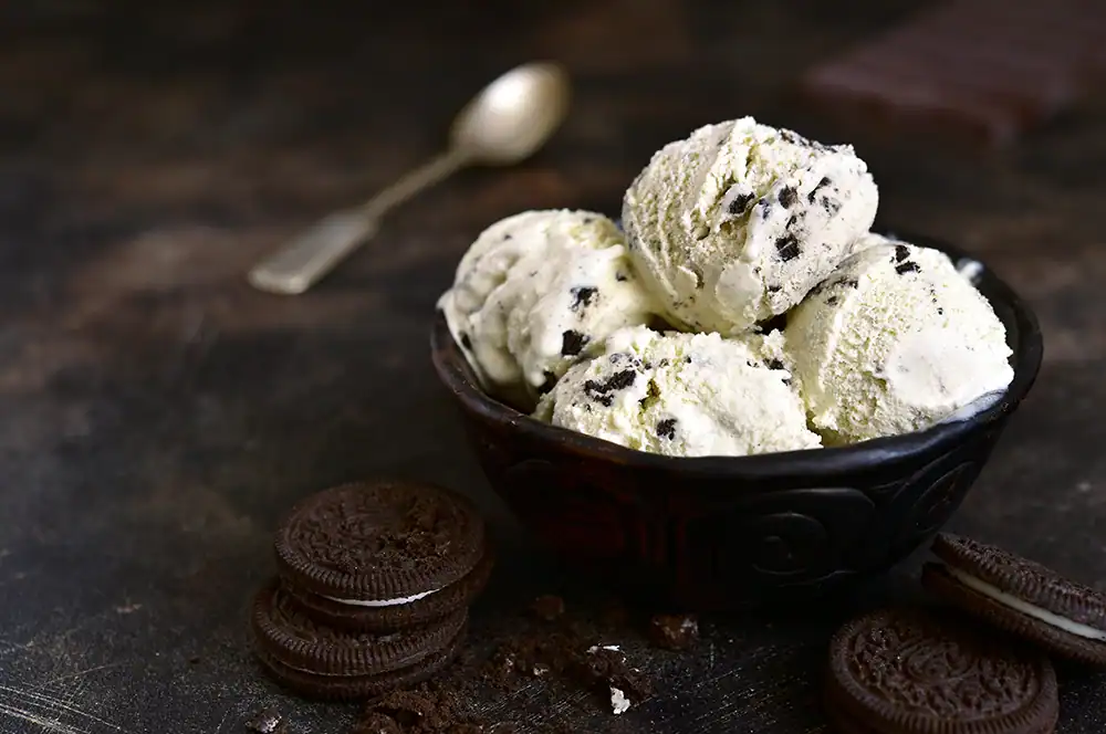 Black bowl filled with scoops of chocolate chip ice cream surrounded by Oreo cookies.