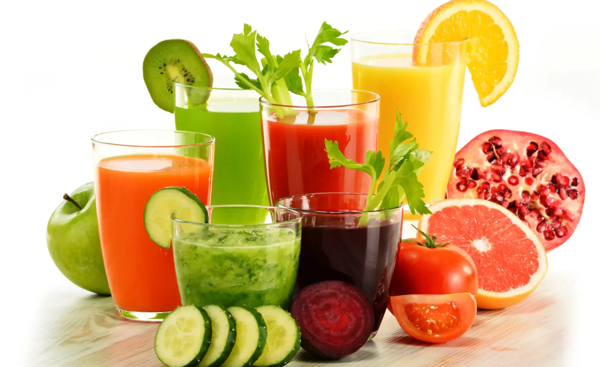 Array of glasses filled with fruit and vegetable juices surrounded by cut fruits